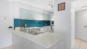 A modern kitchen with a central island, white cabinetry, and a blue backsplash. - Unit 13 Charlton on the Esplanade (Torquay)