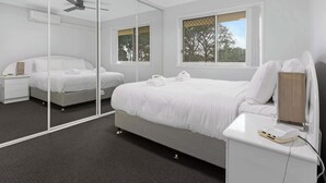 A modern bedroom with a large bed, a bedside table, a mirror, and a ceiling fan. - Unit 13 Charlton on the Esplanade (Torquay)