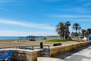 Eine Strandpromenade mit freiem Blick auf das Meer, Palmen und ein weiter Pier im Hintergrund.