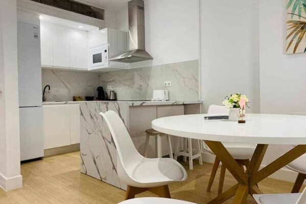 A modern kitchen with white cabinets, a marble backsplash, and a round dining table with white chairs.