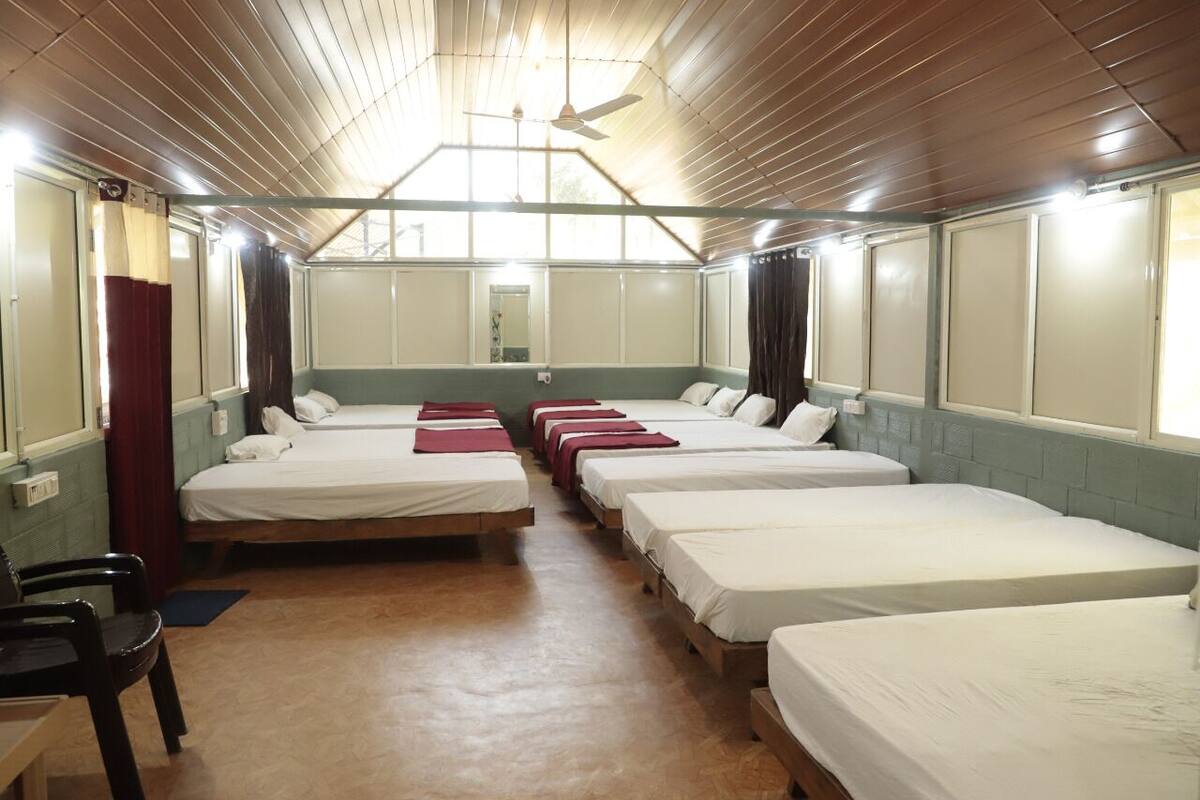A dormitory room with multiple beds, a ceiling fan, and a window.
