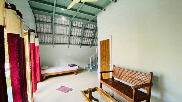 A room with a bed, a wooden bench, a ceiling fan, and a staircase leading to an upper level. - Falling Water Resort by Travent Mug (Sakleshpur)