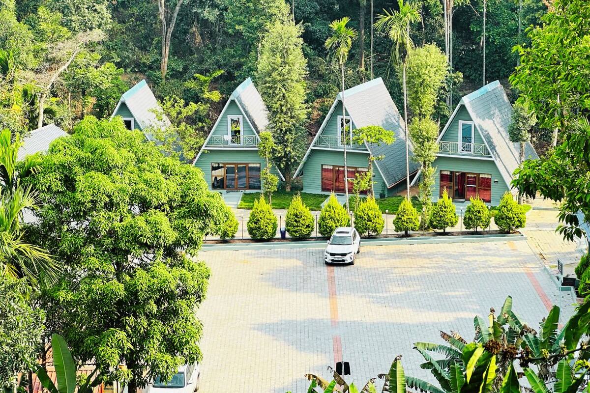A row of green-roofed cottages with a paved driveway and lush greenery surrounding them.