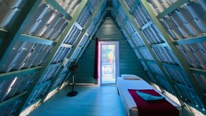 A triangular attic room with a bed, a fan, and a door leading outside.