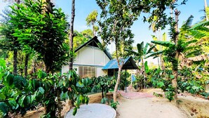 A house surrounded by lush greenery, a concrete circular structure, and a small building with a blue roof.