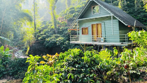 A house with a balcony, surrounded by lush greenery and a river.
