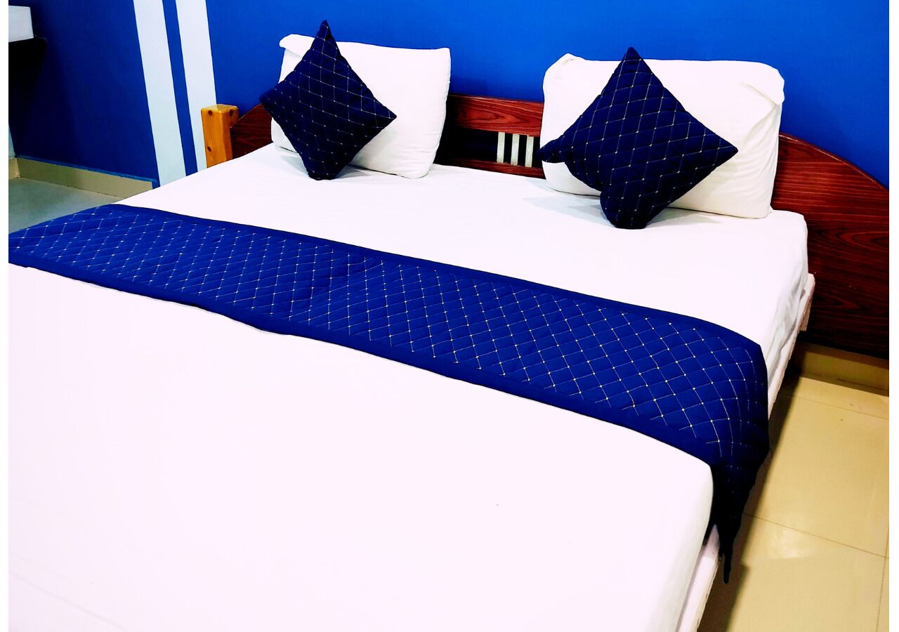 A bed with a blue quilt and two pillows, a wooden headboard, and a blue wall.