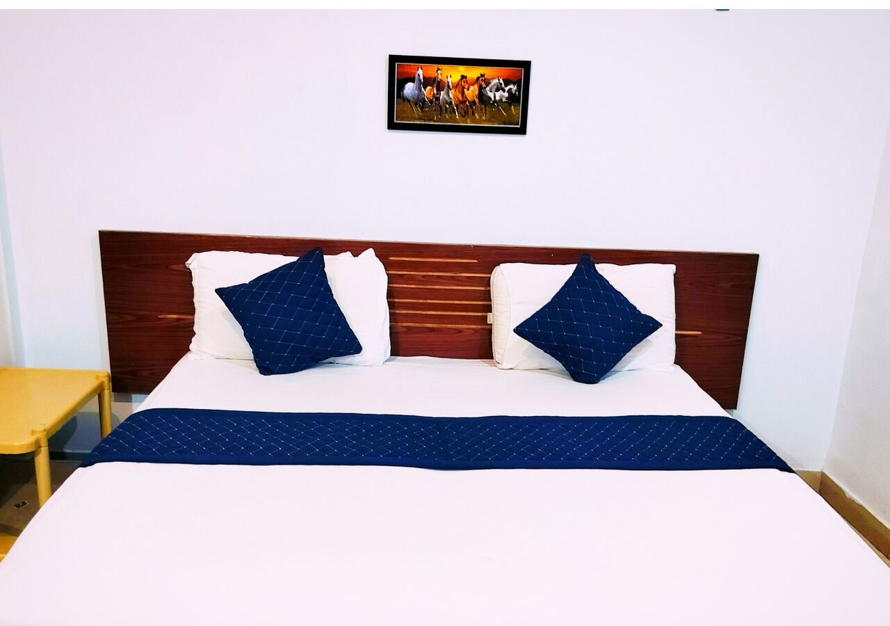 A bed with a wooden headboard, two pillows, a blue blanket, and a painting above the bed.