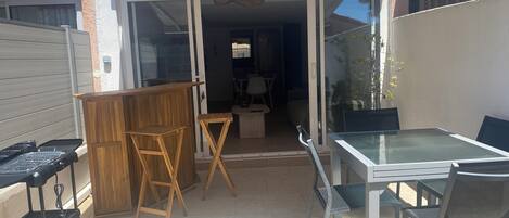 A patio area with a glass table and chairs, a wooden bar, and a grill.