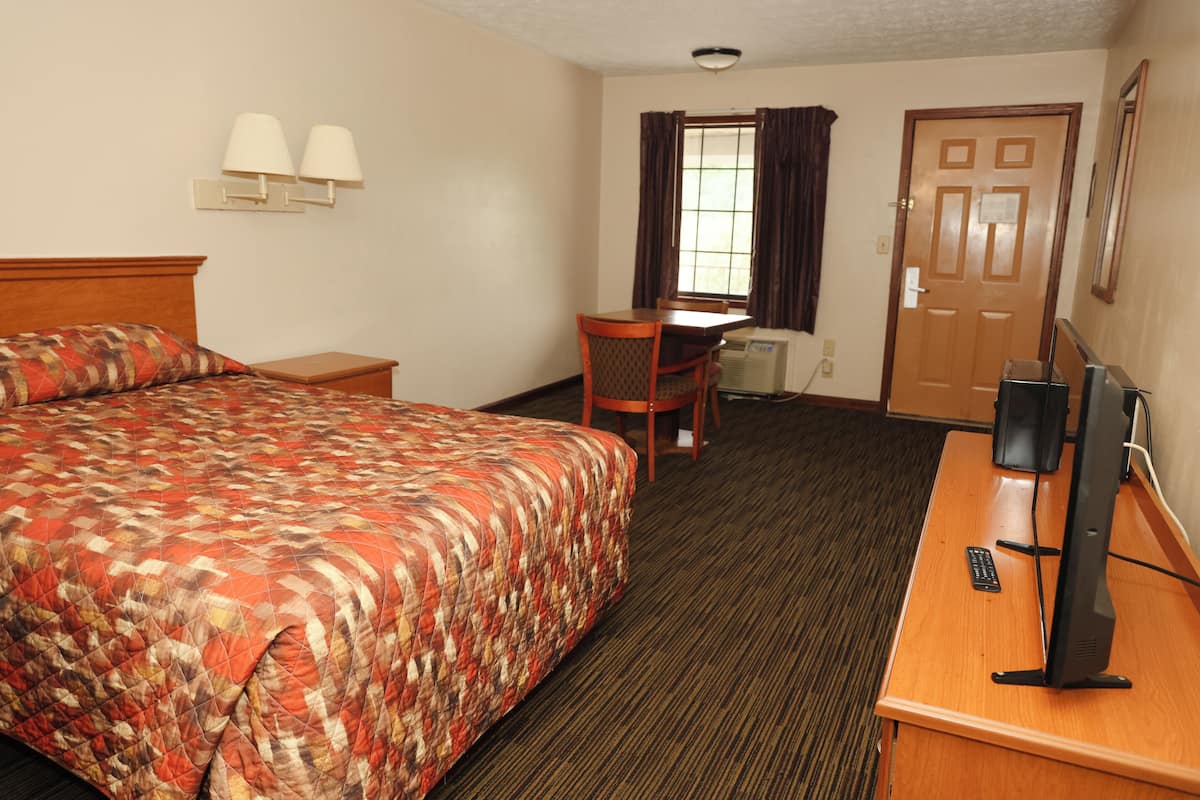 Quarto de hotel com cama, escrivaninha com computador, cadeira e janela com cortinas.