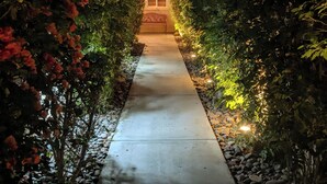 A pathway flanked by red flowers and green foliage leading to a building with a window and a door. - NEW Modern 3bd Home in Palm Springs,PGA Country Club the Ultimate Retreat (Cathedral City)
