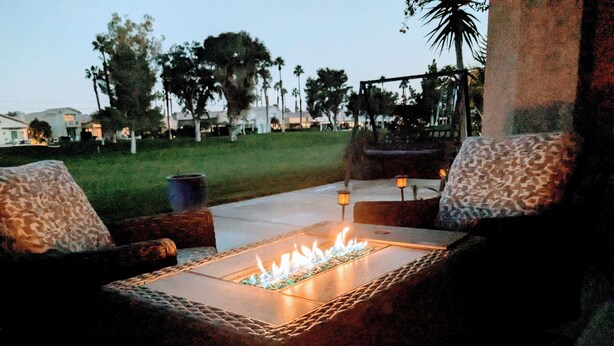 An outdoor seating area with a fire feature, surrounded by a stone wall and palm trees. - NEW Modern 3bd Home in Palm Springs,PGA Country Club the Ultimate Retreat (Cathedral City)