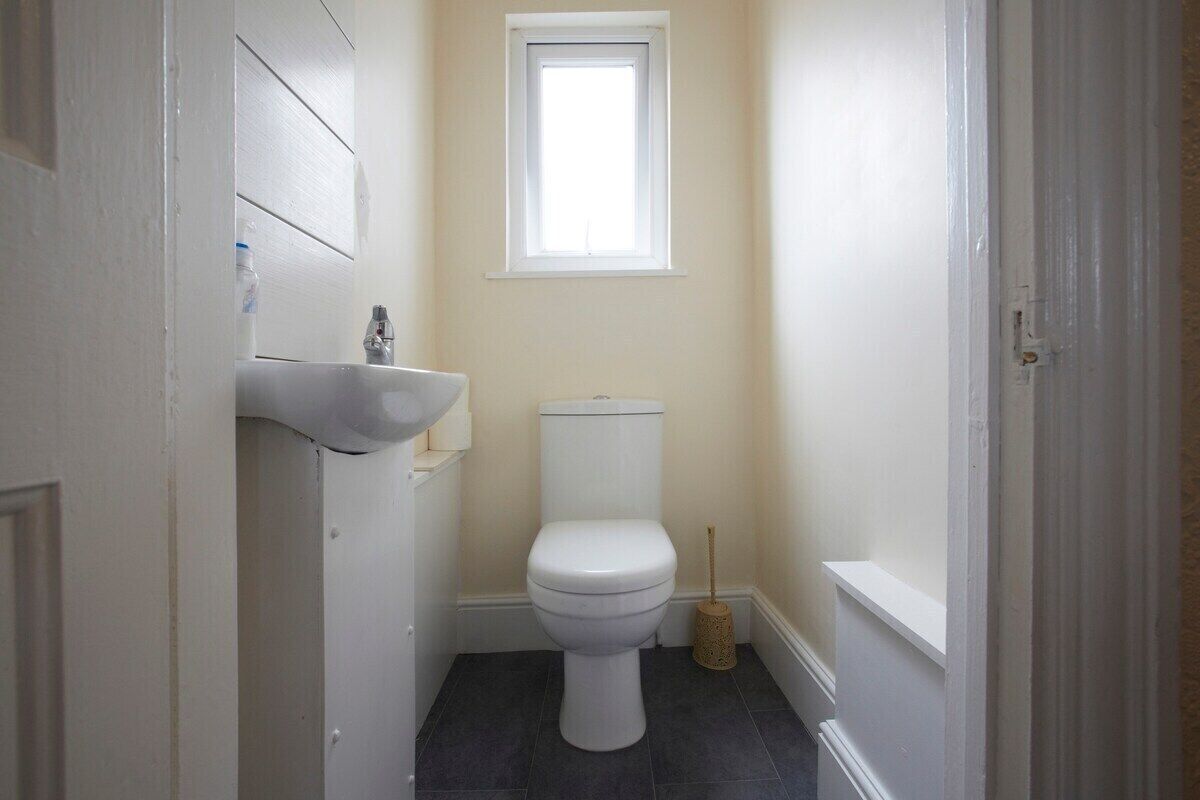 Un baño pequeño con un inodoro blanco, un lavabo blanco y un ventanal sobre el inodoro.