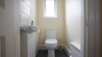 Un baño pequeño con un inodoro blanco, un lavabo blanco y un ventanal sobre el inodoro.