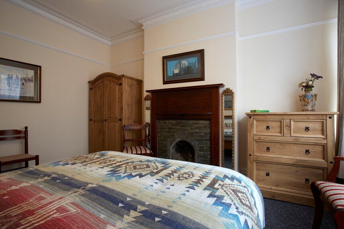 A bedroom with a large bed, a wooden wardrobe, a fireplace, and a dresser.