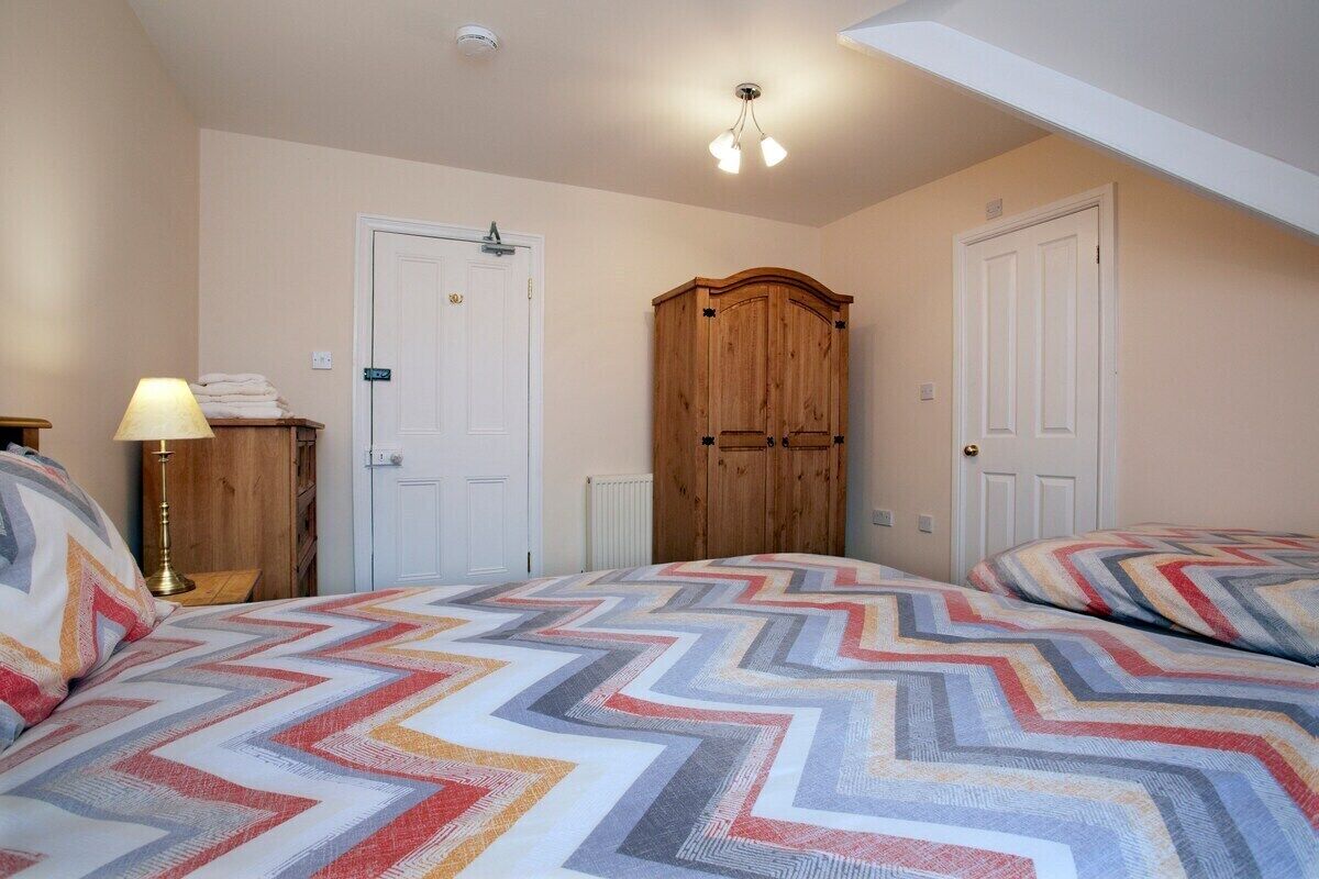 A bedroom with two beds, a wooden wardrobe, and a ceiling light fixture.