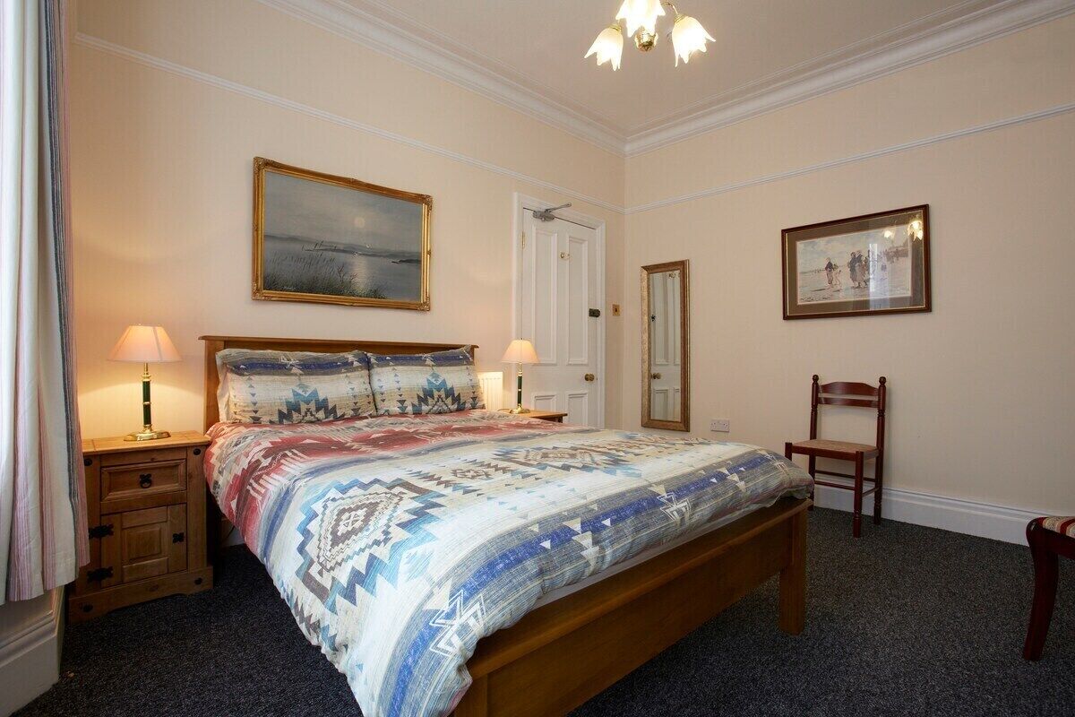Une chambre à coucher avec un grand lit, deux tables de chevet avec des lampes, une chaise et deux tableaux encadrés accrochés aux murs.