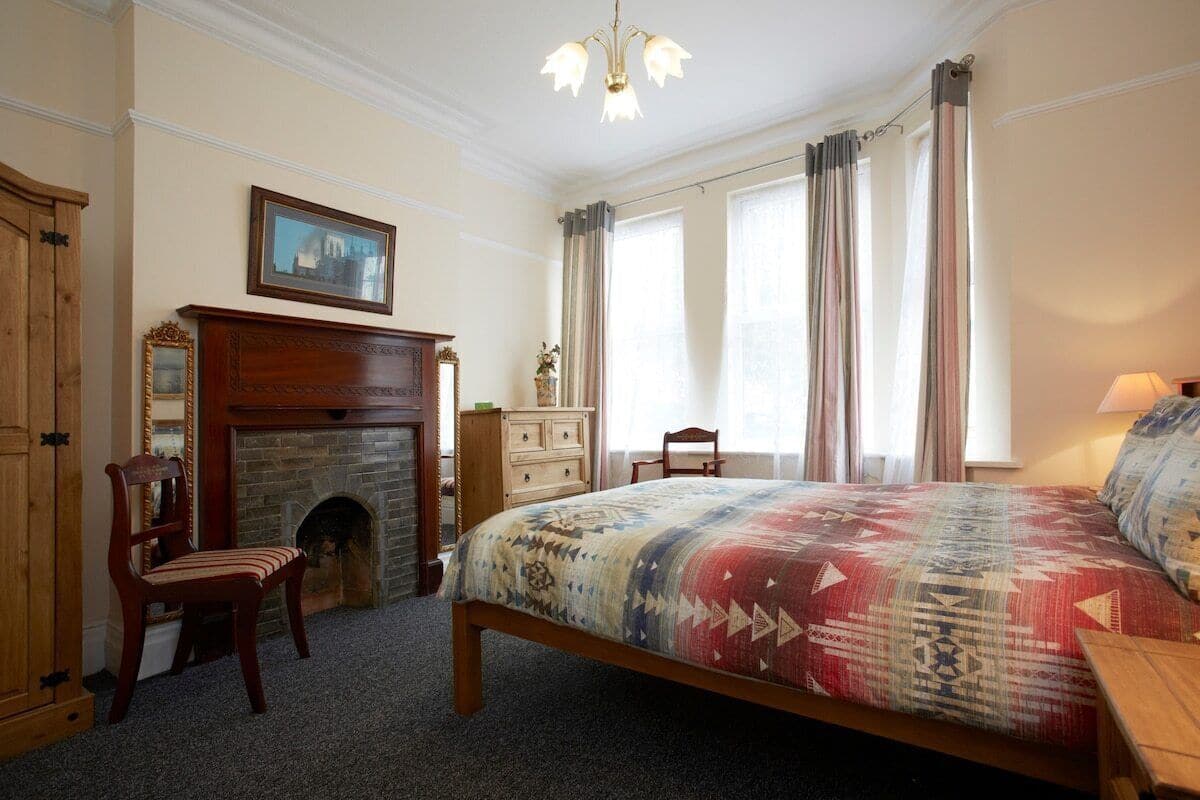 A bedroom with a large bed, a fireplace, a wooden chair, and a dresser.