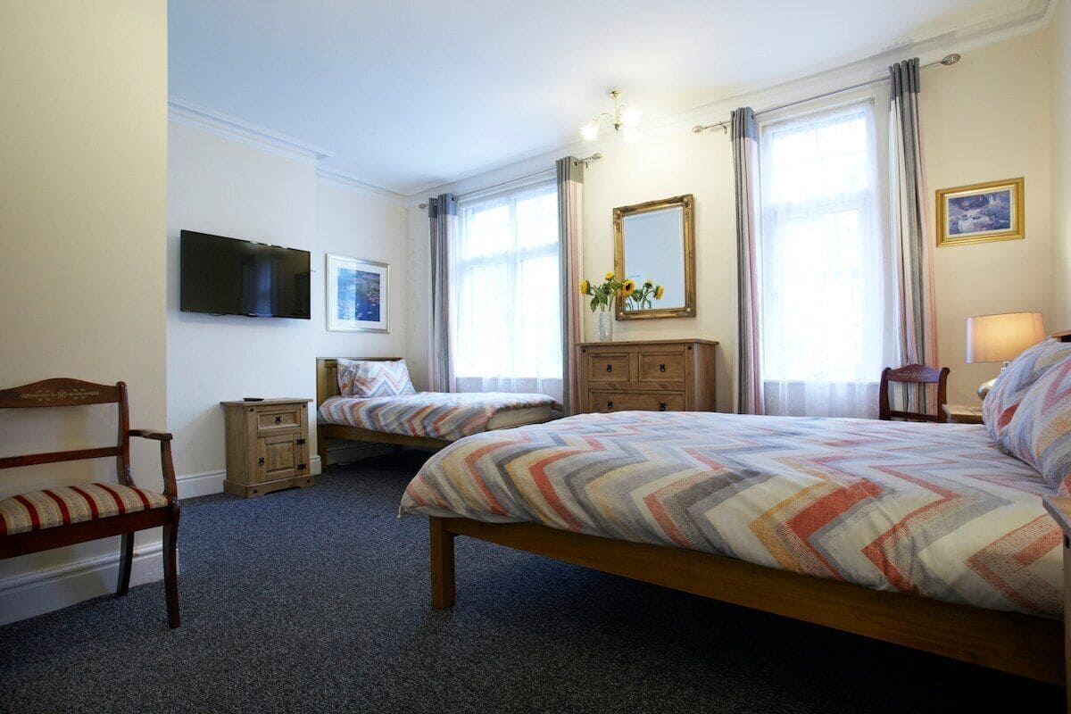A bedroom with two single beds, a wooden chair, a television, a mirror, and a window with curtains.