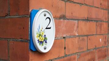 A house number plaque with a floral design on a brick wall.