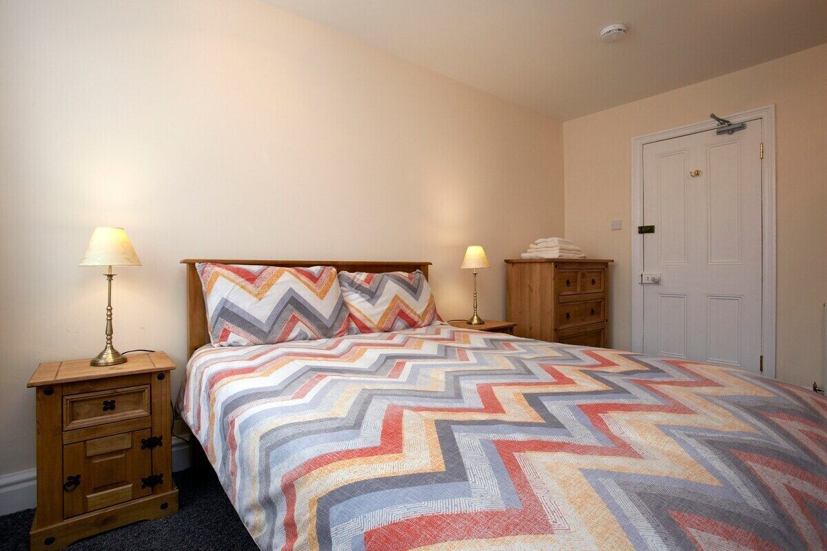 A bedroom with a bed, two bedside tables, a nightstand, a wardrobe, and a door.