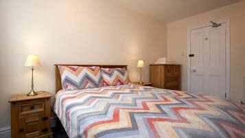 A bedroom with a bed, two bedside tables, a nightstand, a wardrobe, and a door.