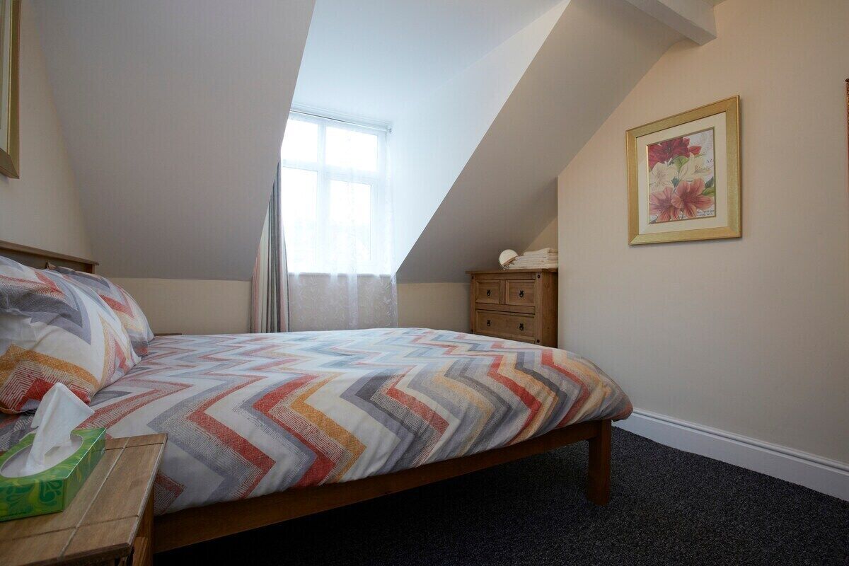 A bedroom with a bed, a nightstand, a window, a dresser, and a framed picture on the wall.