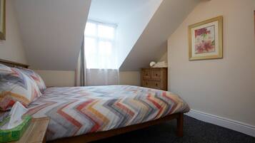 A bedroom with a bed, a nightstand, a window, a dresser, and a framed picture on the wall.