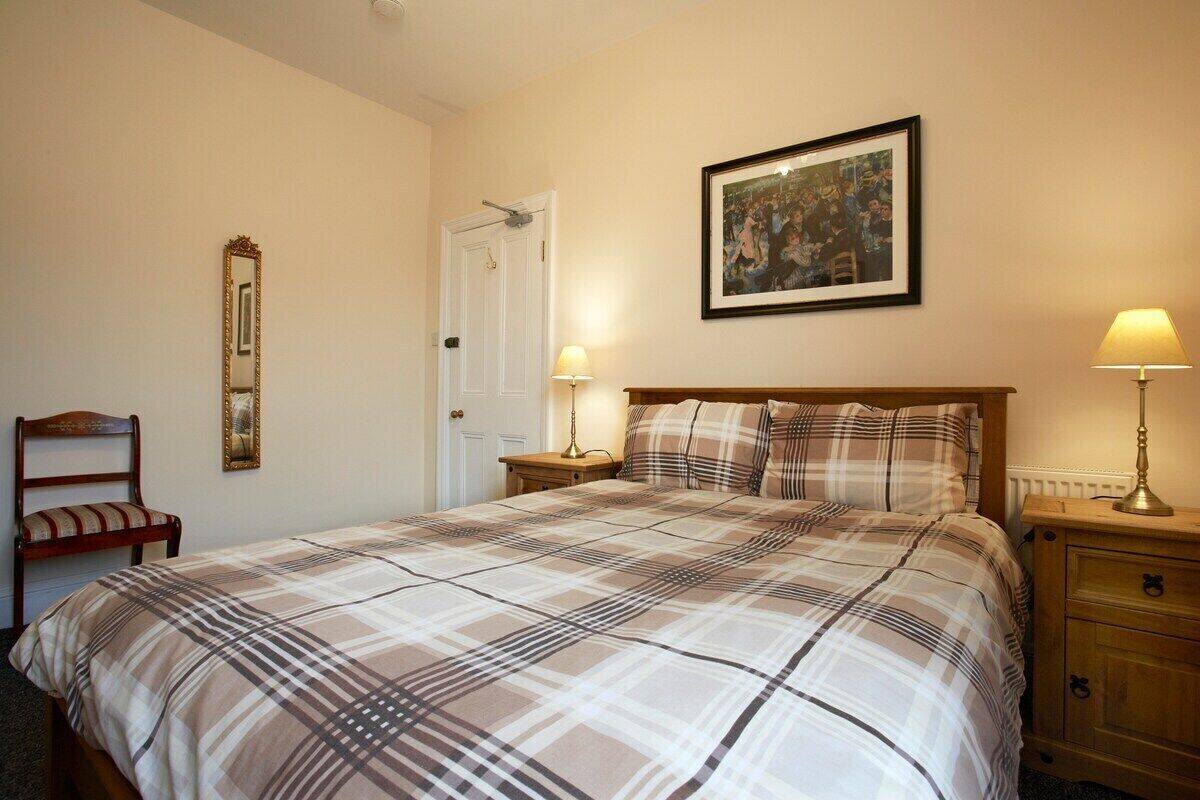 A bedroom with a large bed, a nightstand, a chair, a mirror, and a framed picture on the wall.