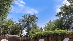 A backyard with a wooden fence, three Adirondack chairs, and a grill.