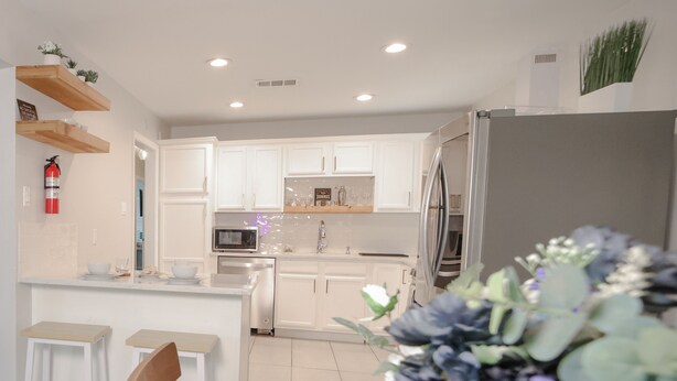 A modern kitchen with white cabinets, a microwave, and a refrigerator. There is a dining table with chairs and a vase of flowers.