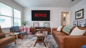 A living room with a large flat-screen TV mounted on the wall displaying "NETFLIX".