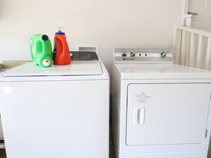 Un lave-linge à chargement frontal et un sèche-linge placés côte à côte, avec des bouteilles de lessive posées sur le dessus.