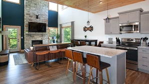 A modern kitchen with a stone fireplace, bar stools, and stainless steel appliances. - 5BR Retreat Near Dollywood, w Hot Tub & Game Room! (Pigeon Forge)