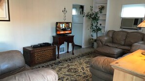 Una sala de estar con televisor, sofás de cuero, un mueble de madera y un tapiz estampado.