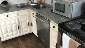 Una cocina con muebles blancos, un lavavajillas de acero inoxidable, un microondas y una estufa.