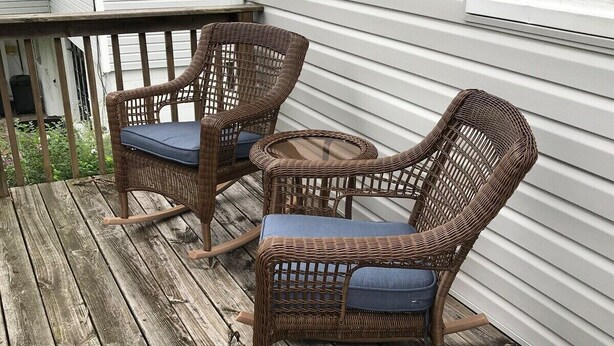 Una terraza de madera con mecedoras de mimbre y una mesita.