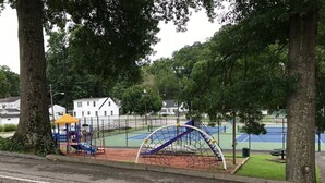 Un parque infantil con una estructura para escalar, una cancha de baloncesto y una cancha de tenis.