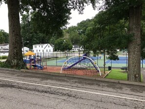 A playground with a climbing structure, a basketball court, and a tennis court.