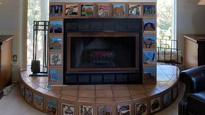 Una sala de estar con chimenea, un cuadro grande sobre ella, y un revestimiento de chimenea con azulejos y diversos diseños.