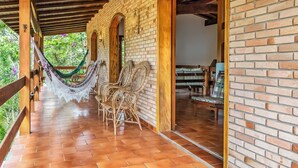 A covered patio with a brick wall, wooden beams, and a hammock. - Villaggio Dei Pini (Ubatuba)
