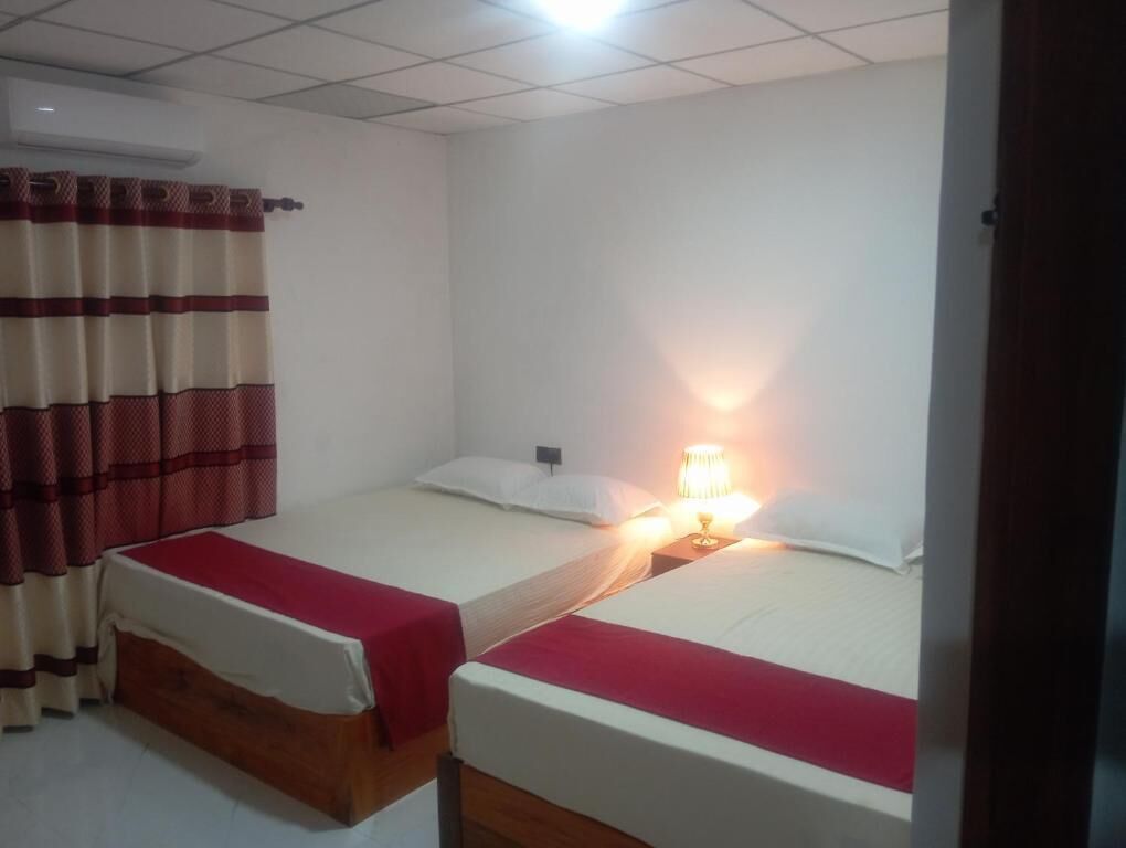 A room with two single beds, a red and white striped curtain, and a bedside lamp.