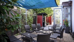An outdoor patio with wicker furniture, a blue canopy, and a red building in the background. - Brauerei Gasthaus Lohhof (Unterschleißheim)