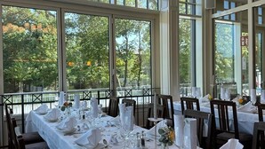 A restaurant with a long table set for a meal, large windows, and a hanging light fixture. - Brauerei Gasthaus Lohhof (Unterschleißheim)