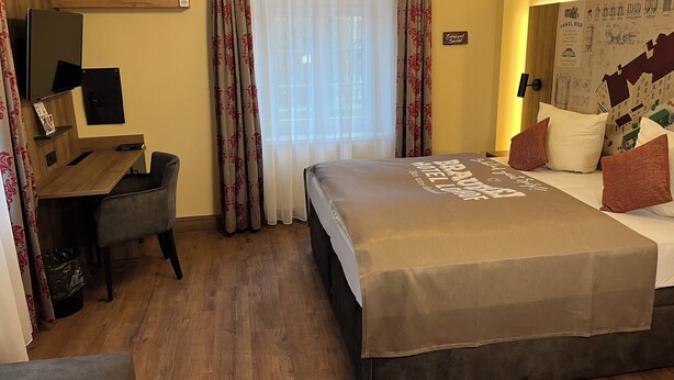 A hotel room with a bed, a desk, a TV, and a window with curtains. - Brauerei Gasthaus Lohhof (Unterschleißheim)