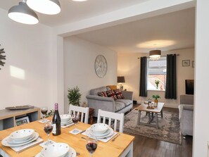 A dining area with a wooden table set for four, a grey sofa, a small side table, and a window with curtains. - Postmans Lodge (Middlesbrough)