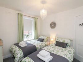 Quarto com duas camas, janela com cortinas, um candelabro e decoração na parede.