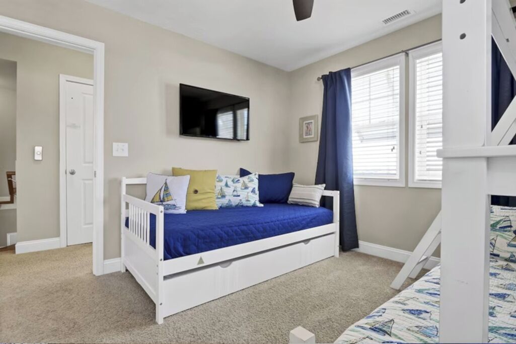 Une chambre avec un lit superposé, un lit simple, un téléviseur à écran plat, une fenêtre avec des rideaux et une porte.
