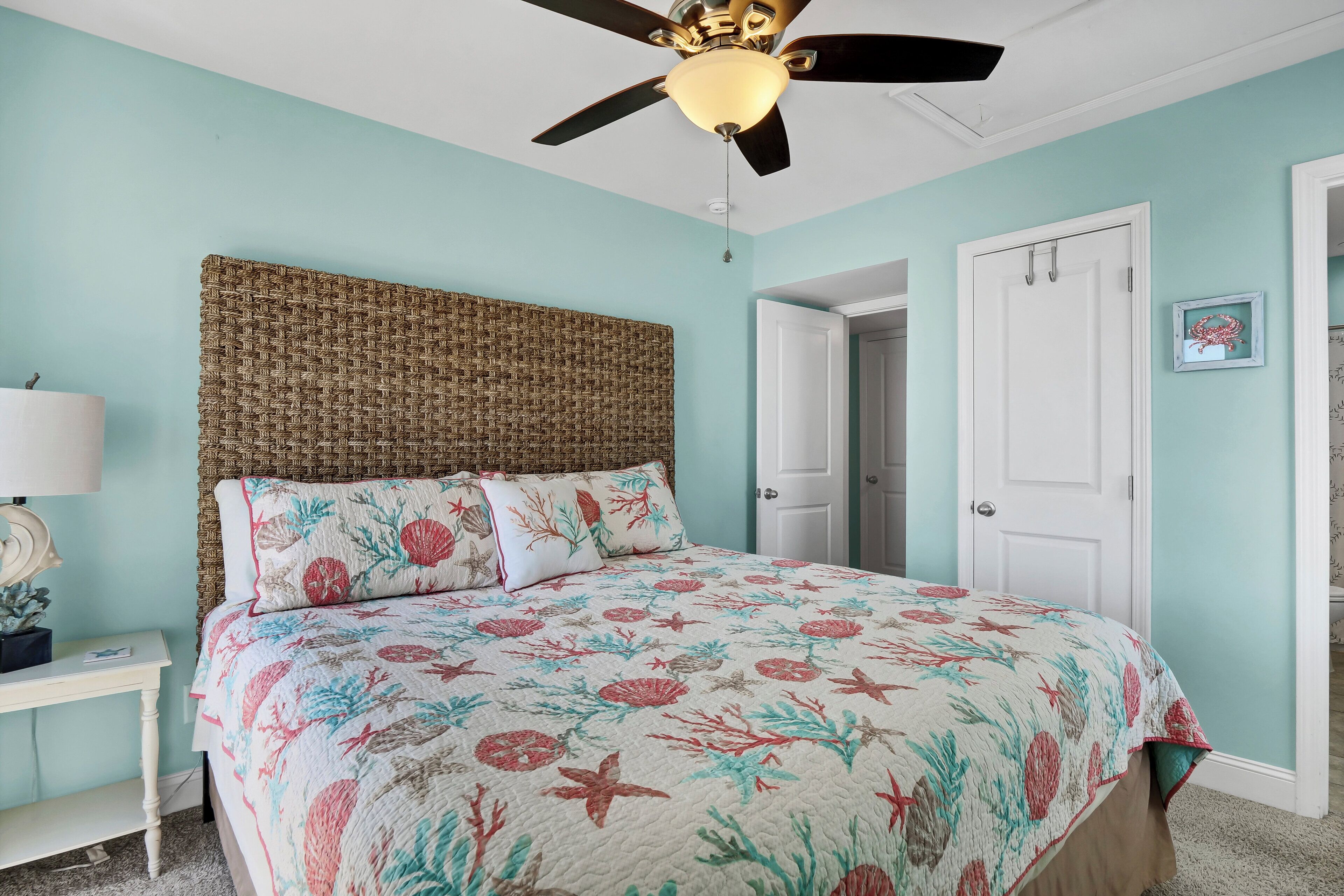 A bedroom with a bed, a ceiling fan, a bedside table, and a door.