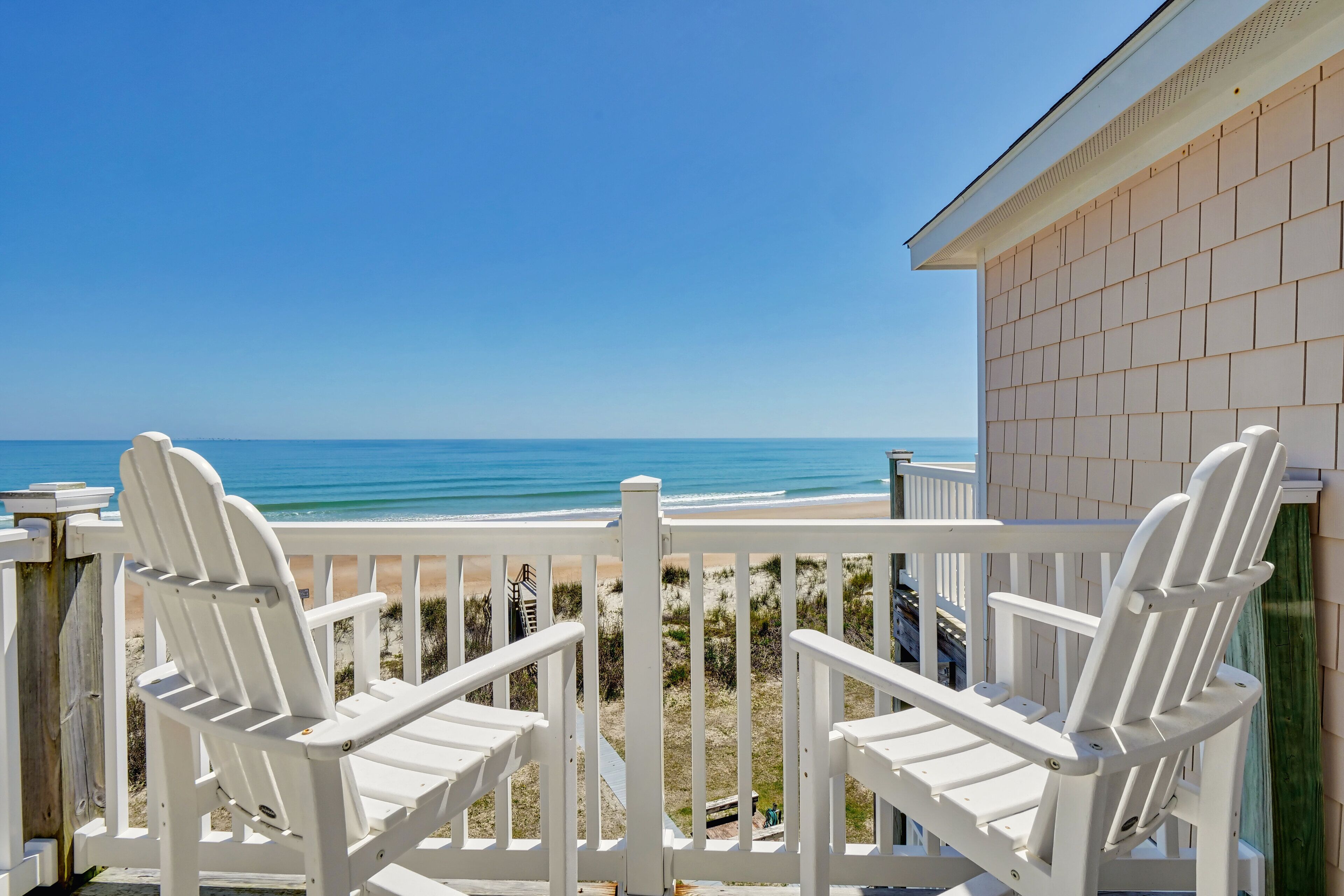 A balcony with white chairs overlooking a beach.